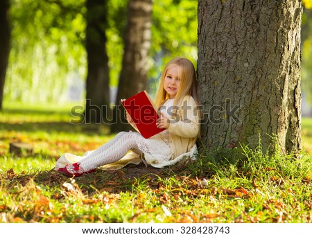 Cute little blonde girl sit near tree, read favorite book and dream