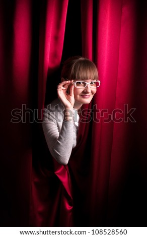 Girl in glasses behind the red curtain