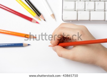 child draws on a white paper with colored pencils, a computer keyboard in the background