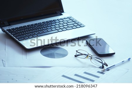 Modern business workplace with tablet, laptop and some papers with charts, graphs and numbers on a desktop.