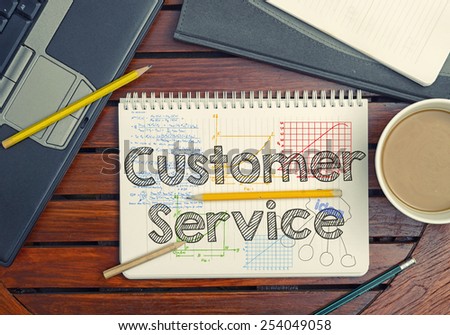 Notebook with text inside Customer Service on table with coffee, notebook and pencils