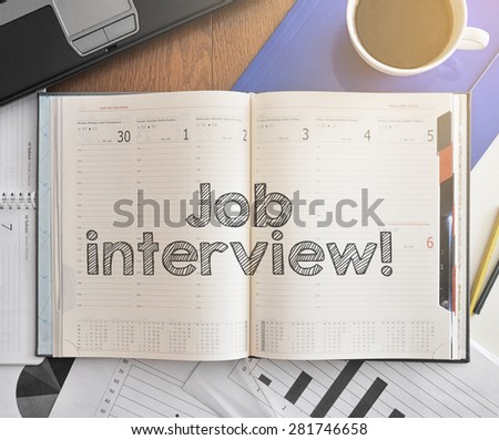 Notebook with text inside Job Interview on table with coffee, some diagrams on paper and laptop