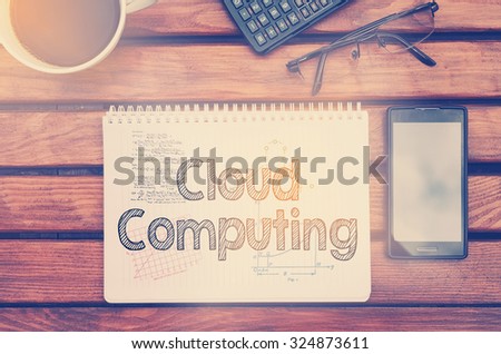Notebook with text inside Cloud Computing on table with coffee, mobile phone and glasses.
