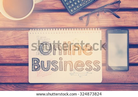 Notebook with text inside Online Business on table with coffee, mobile phone and glasses.