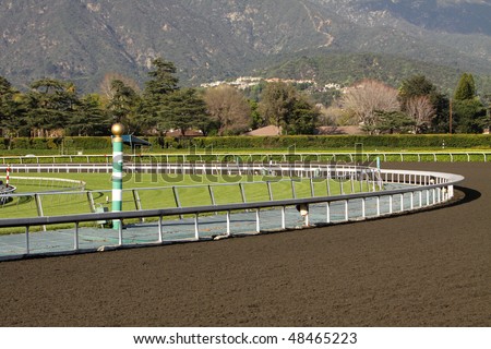 View of a horse racing track with mountains in background. Focus on green and white striped eighth pole.