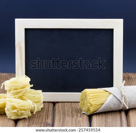 Food cooking concept. Empty blackboard with uncooked italian pasta fettuccine and spaghetti on wooden background