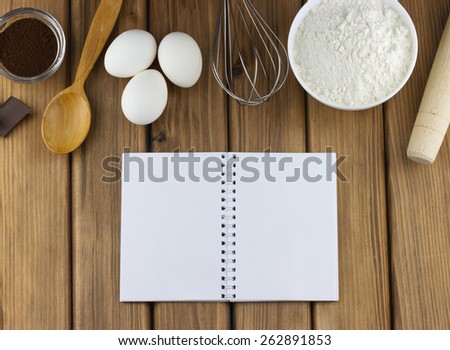 Cooking concept. Top view of food ingredients and kitchen utensils for cooking with blank notebook on wooden background
