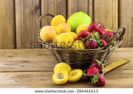 Fresh apricots strawberries and apple in the basket on wooden background