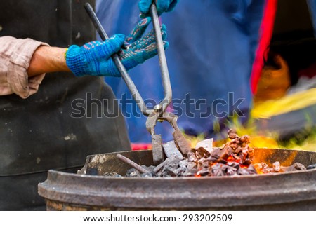 Blacksmith get a hot iron from the fire for forging in outdoor workshop