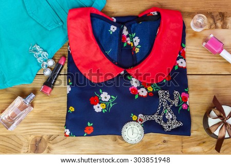 Top view of fashion women's set: denim shorts, blouse, handmade watch, cosmetics and small gift box on wooden background