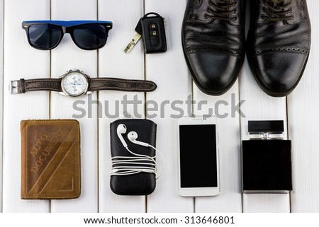 Top view of gentlemanly set: watches, car keys, shoes, sunglasses, smartphone, auto document, player with headphones and perfume on white wooden background