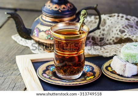 Traditional Turkish tea set: glass cup of tea, painted copper teapot, Turkish delight on a plate on wooden background