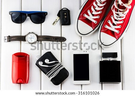 Top view of gentlemanly set: red shoes, car keys, sunglasses, watch, smartphone, player, stick antiperspirant and perfume on white wooden background