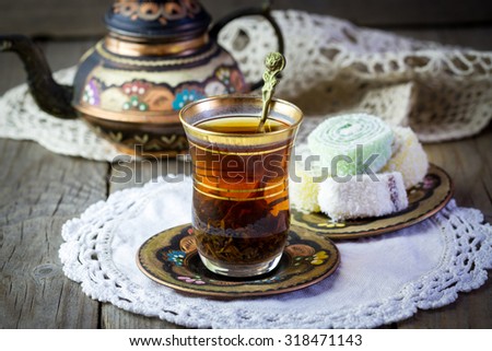 Traditional Turkish tea set: glass cup of tea, painted copper teapot, Turkish delight on a plate and vintage napkin on old wooden table