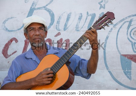 CIENFUEGOS, CUBA - JANUARY 27, 2013: Old man plays guitar on street of Cienfuegos,Cuba. In background comunism propaganda paint on street wall.