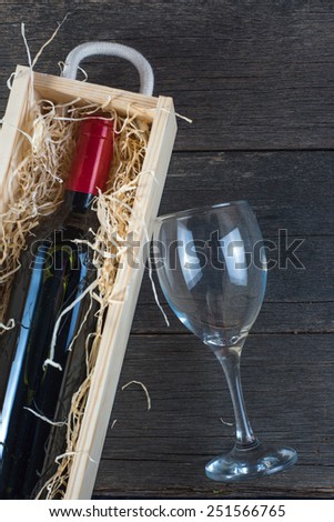 Bottle of red wine in case and glass on rustic wood