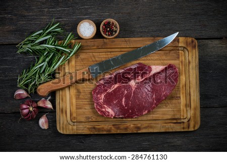 Raw rib eye beef steak with herbs and spices from above on wooden rustic table
