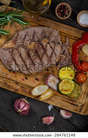 Grilled rib eye beef steak with roasted vegetables on wooden rustic board from above