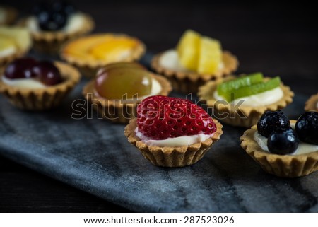 Mini pastry tartlets with fresh fruits, on marble serving board