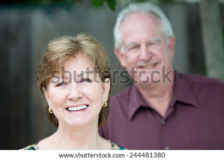 Portrait of older couple outdoors smiling at camera with woman in front in focus.