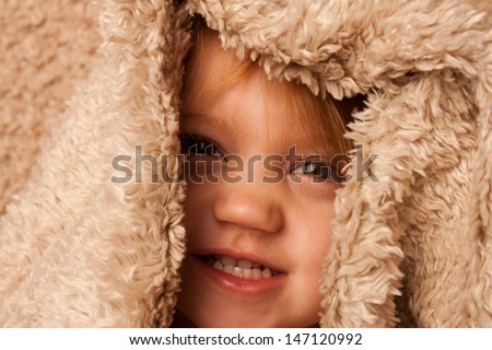 Smiling toddler hiding in fur blanket