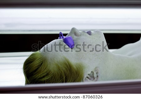 Red haired young woman wearing goggles in lit tanning bed