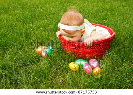 Baby in red basket peeking over the side at an assortment of Easter eggs