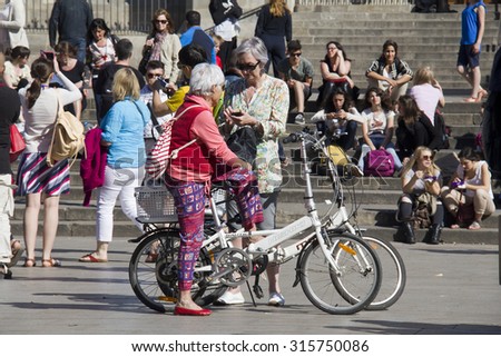 Barcelona, Spain - May 22, 2015: Two older ladies with bikes and other tourists near the steps of the cathedral of Barcelona, Spain on May 22, 2015.
