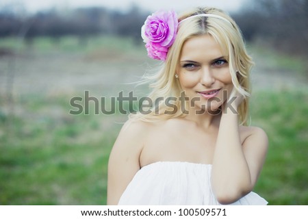 Portrait of beautiful young blond woman in white blouse at park holding her neck