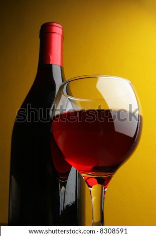 Still-life with glass and bottle of red wine over yellow background