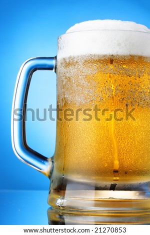 Mug of beer close-up with froth over blue background