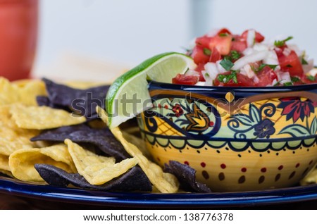 A fancy bowl with nacho corn chips and fresh onion tomato salsa