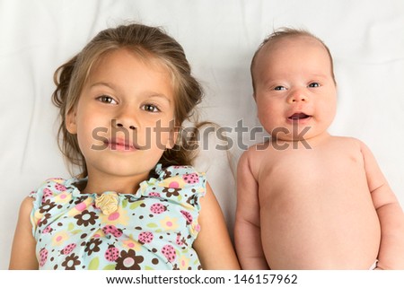 Little girl lying with her newborn sister on a white blanket