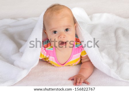 Little baby girl with her head covered by terry towel is trying to crawl while looking at the camera