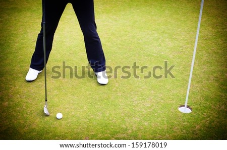 Golf player training putting ball in cup on green