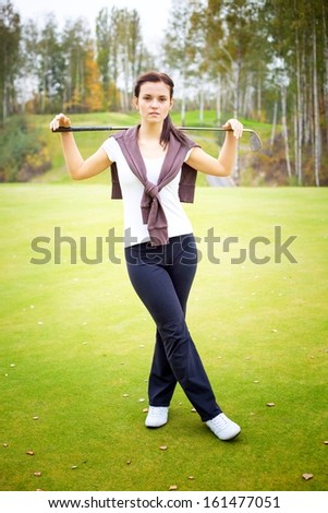 Young woman golf player posing on green with club and ball