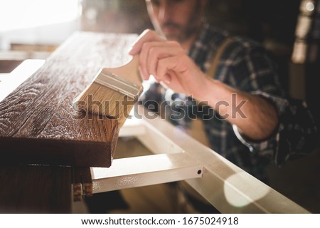 Close up of paintbrush applies paint or varnish on wooden board in carpentry workshop Foto stock © 