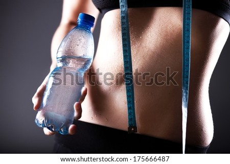 Fitness woman wet sporty belly after exercise with measuring tape and water bottle