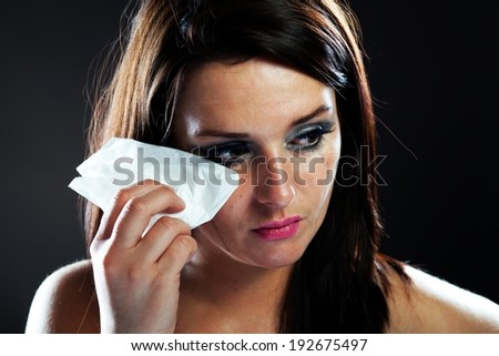 Hurt woman crying, face with smeared make up on dark background