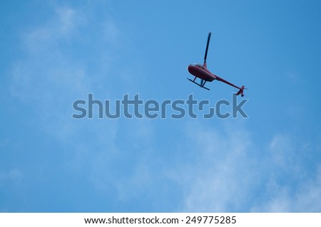 Helicopter high above on blue sky. Red helicopter without logos on blue sky.