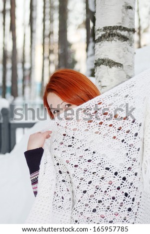 Cute girl hides her face behind shawl near birch at winter forest.
