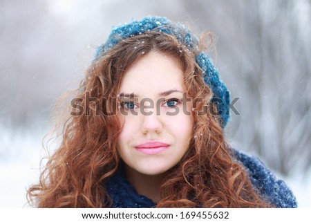 Beautiful girl in blue beret looks at camera outdoor at winter day in park
