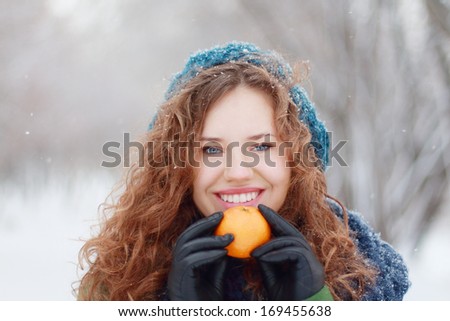Beautiful girl in blue beret holds mandarin and smiles outdoor at winter day in park