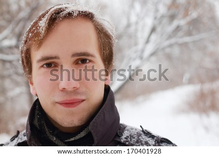 Young man with snowflakes in hair looks at camera at winter snowy day