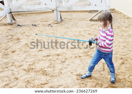 Pretty little happy girl standing on sand with blue rapier training for fencing