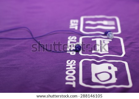 Vacuum blue headphones lying on purple T-shirt with text eat, sleep, shoot