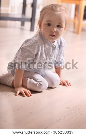 Little cute blond girl in striped shirt sitting on wooden floor