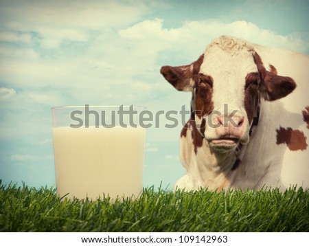 Milk in glass on grass with cow and sky in background