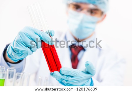 scientist working in the lab, in protective mask and cap, examines a test tube with liquid
