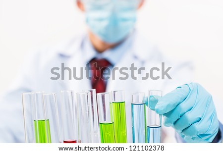 scientist working in the lab, in protective mask and cap, examines a test tube with liquid